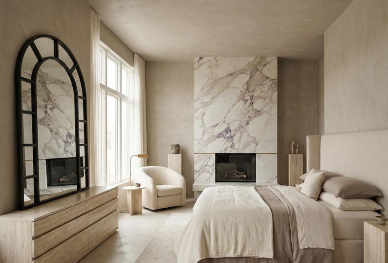 May include: A bedroom featuring a large arched floor mirror with a black frame, a light wood dresser, a cream-colored armchair, a marble fireplace, and a bed with neutral-toned bedding. The room has light-colored walls and large windows.
