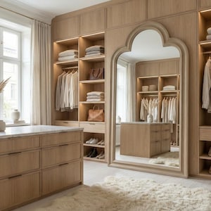 May include: A light wood walk-in closet with built-in shelving, drawers, and a large mirror. The closet features hanging clothes, folded towels, and handbags. A white marble-topped dresser and a fluffy rug complete the space.