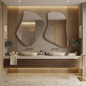 Könnte beinhalten: Ein modernes Badezimmer mit zwei einzigartig geformten, goldgerahmten Spiegeln. Der Waschtisch verfügt über zwei Steinbecken, einen dunklen Holzschrank und eine hellfarbige Arbeitsplatte. Dekorative Pflanzen und Handtücher tragen zum Spa-ähnlichen Ambiente bei. Der Boden ist ein gesprenkelter beigefarbener Fliesenboden.