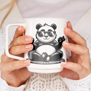 May include: White ceramic mug with a black and white illustration of a panda wearing sunglasses and sitting in a meditative pose. The panda is sitting on a platform with a wood grain pattern.
