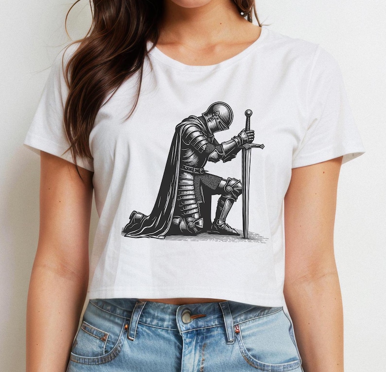 May include: A white cropped t-shirt with a black and white illustration of a knight kneeling with a sword. The knight is wearing armor and a cape.