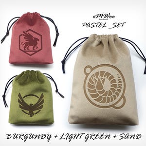 May include: Set of three velvet dice bags in burgundy, light green, and sand colors. Each bag features a different embroidered design: a griffin, a bird with wings spread, and a spiral.