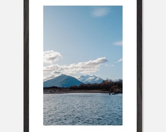 May include: A scenic photograph of a mountain range with snow-capped peaks reflected in a still lake. The sky is a clear blue with fluffy white clouds.