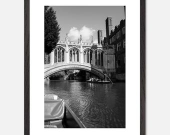 Op de afbeelding: Een zwart-witfoto van een brug over een rivier. De brug is van steen en heeft een reeks bogen. Aan beide kanten van de rivier staan gebouwen. Een boot ligt in de rivier.