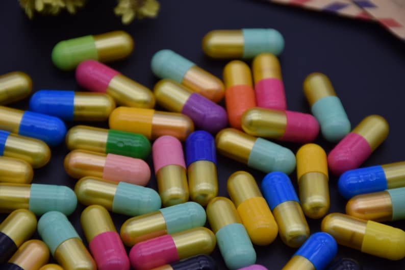 May include: A collection of colorful capsules with gold accents. The capsules are arranged in a random pattern on a black surface.