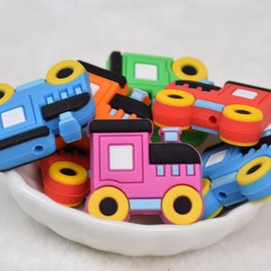 Puede incluir: Una colección de vagones de tren de juguete coloridos en un cuenco blanco. Los trenes son de varios colores, incluyendo azul, rojo, verde y naranja, con ruedas amarillas. Cada tren tiene un diseño único, perfecto para niños.
