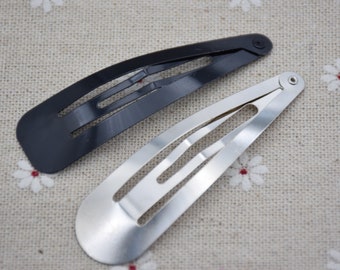 May include: Two hair clips, one black and one silver, on a white fabric background with a floral pattern.