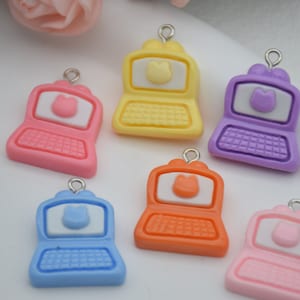 Puede incluir: Seis encantos de plástico de color para portátil con una cara de gato en la pantalla. Los encantos son de color rosa, amarillo, morado, naranja, azul y rosa claro.