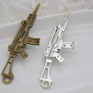 May include: Two metal gun charms, one silver and one bronze, with a detailed design. The charms are perfect for adding a unique touch to jewelry or crafts.