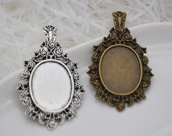 May include: Two oval-shaped pendant trays with ornate silver and bronze frames. The frames feature a floral design with leaves and swirls. The trays are blank and ready for embellishment.