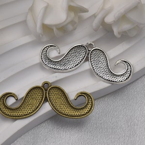 May include: Two metal mustache charms, one silver and one bronze, with a textured surface. The charms are on a white background.
