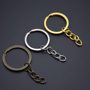 Könnte beinhalten: Drei Schlüsselringe mit befestigten Ketten. Die Schlüsselringe sind silber, gold und bronzefarben. Die Ketten sind silber, gold und bronzefarben.