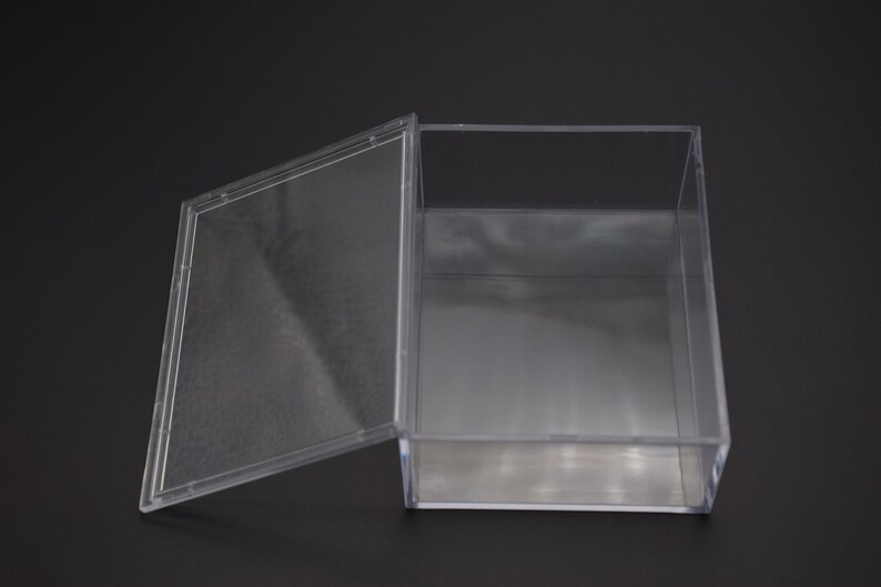 May include: A clear plastic box with a hinged lid. The box is empty and has a rectangular shape.