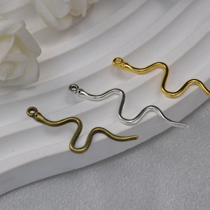 May include: Three snake-shaped metal charms in gold, silver, and bronze. The charms are all in the shape of a snake with a curled tail. They are perfect for adding a touch of whimsy to jewellery or crafts.