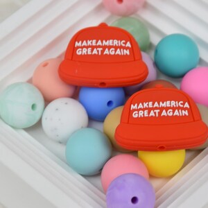 May include: A collection of colorful silicone beads with two red silicone beads shaped like baseball caps with the text "Make America Great Again" in white.