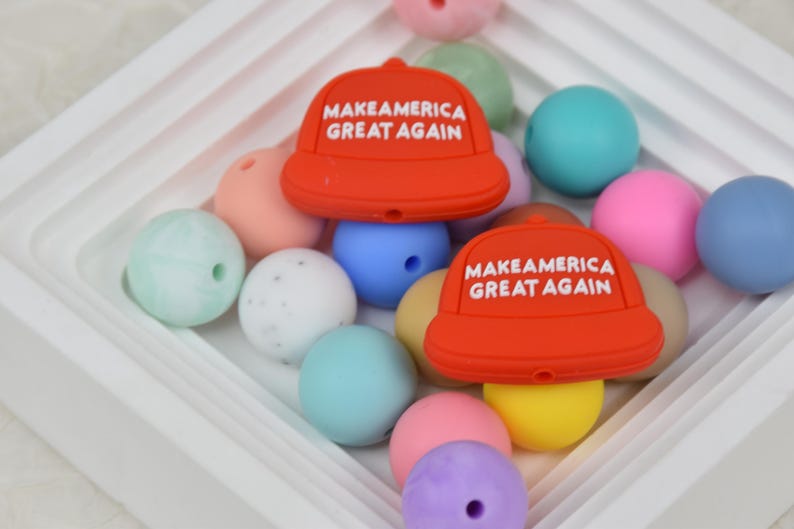May include: A collection of colorful silicone beads with two red silicone beads shaped like baseball caps with the text "Make America Great Again" in white.