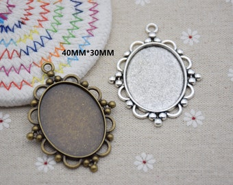Puede incluir: Dos colgantes ovalados, uno en tono bronce y otro plateado, con bordes decorativos y presillas para colgar. El texto "40mm*30mm" es visible. Ideales para la creación de joyas.