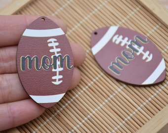 Könnte beinhalten: Zwei braune und weiße fußballförmige Ornamente mit dem Wort "mom" in schwarzer und gelber Schrift.