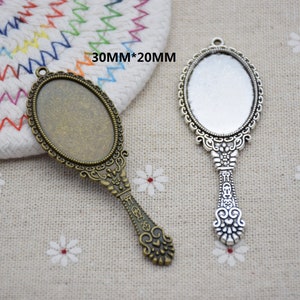 May include: Two ornate silver-tone and bronze-tone hand mirror charms with a 30mm x 20mm oval glass insert. The mirrors have a detailed filigree design and are perfect for adding a vintage touch to jewellery projects.