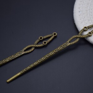 May include: Two antique gold hair sticks with intricate swirling designs. The sticks are about 10 inches long and have a decorative loop at the top.