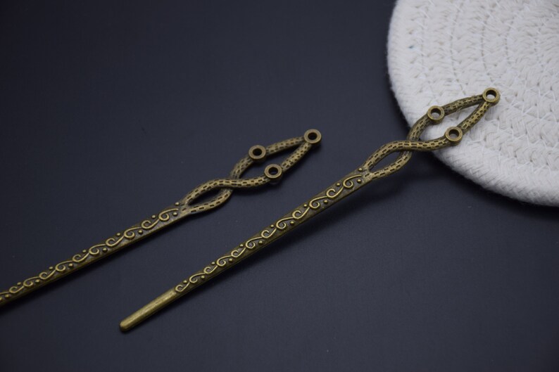 May include: Two antique gold hair sticks with intricate swirling designs. The sticks are about 10 inches long and have a decorative loop at the top.