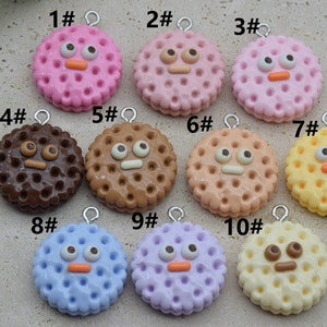 May include: Ten colorful, round, double-layered, polymer clay cookie charms with different facial expressions. Each charm has a silver loop for hanging. The charms are numbered 1 through 10.