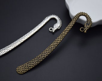 May include: Two dragon-shaped bookmarks, one silver and one bronze, with a textured surface. The bookmarks are curved and have a dragon head at the top.