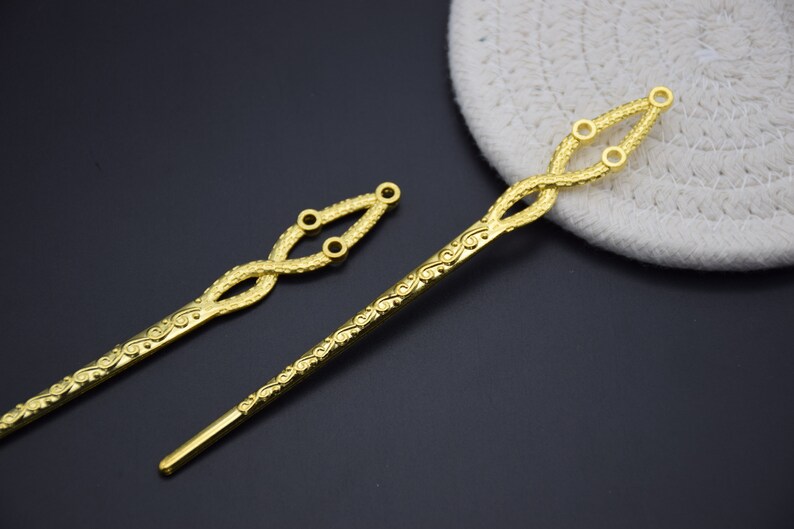 May include: Two gold hair sticks with intricate designs. The sticks are about 10 inches long and have a decorative, twisted design at the top. The sticks are perfect for adding a touch of elegance to any hairstyle.