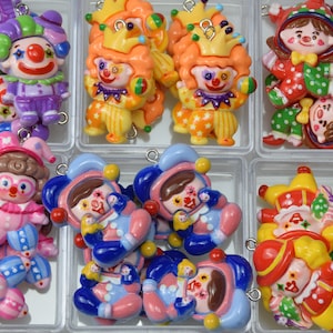 May include: A selection of colourful clown-themed charms in various designs. The charms feature clowns in purple, orange, red, pink, and blue outfits, some with crowns or hats. Each charm has a small metal loop for attaching to jewellery or crafts.