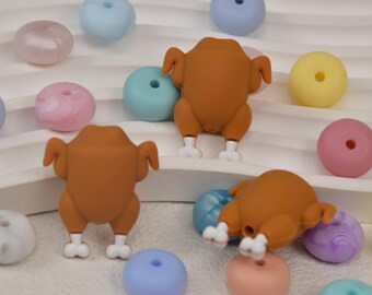 May include: A collection of colourful beads and small brown turkey figurines. The beads are in pastel shades of pink, blue, yellow, and purple. The turkeys have white feet and are arranged on a white surface.