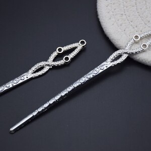 May include: Two silver hair sticks with intricate designs. One stick has a decorative knot at the top with three small holes. The other stick has a more simple design.