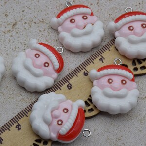 Puede incluir: Una colección de dijes de cabeza de Papá Noel. Cada dije presenta un gorro rojo, cara rosa, barba blanca y un pequeño lazo plateado para sujetar. Un tema festivo navideño.