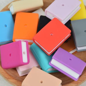 Könnte beinhalten: Eine Sammlung bunter, silikonbuchförmiger Charms mit einem weißen Zentrum. Die Charms sind auf einer Holzoberfläche angeordnet.