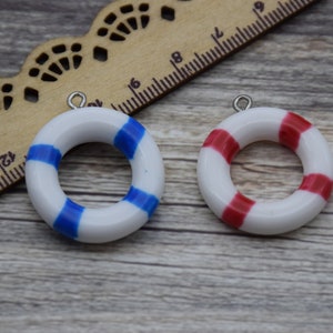 Puede incluir: Dos dijes de salvavidas de cerámica blanca con rayas azules y rojas. Los dijes tienen un lazo plateado para colgar.