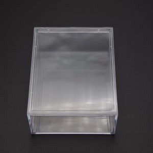 May include: A clear plastic box with a hinged lid. The box is empty and has a rectangular shape.