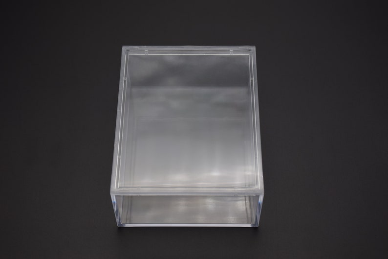 May include: A clear plastic box with a hinged lid. The box is empty and has a rectangular shape.