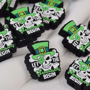 May include: Black and green St. Patrick's Day charms with a skull wearing a green leprechaun hat and the text "LET THE Shenanigans BEGIN". The charms are made of a rubbery material.