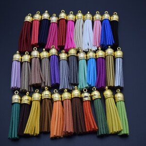 May include: A collection of 30 colourful suede tassels with gold metal tops. The tassels are arranged in rows and are all the same size.