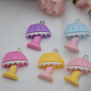 May include: A collection of colorful miniature lamp charms. Each charm features a lamp design with a scalloped lampshade and a base, in shades of pink, yellow, purple, and blue. They have a silver loop for attaching to jewelry or other crafts.