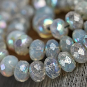 May include: A strand of iridescent white glass beads with a faceted, rounded shape. The beads have a subtle shimmer and are strung together on a clear thread.