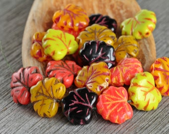 Puede incluir: Surtido de cuentas de vidrio en forma de hoja de colores vivos, en tonos de amarillo, naranja, rojo, verde y negro. Las cuentas tienen forma de hojas de arce y un acabado brillante.
