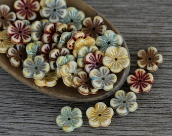 Puede incluir: Una colección de cuentas de colores en forma de flor en tonos crema, marrón, rojo y azul. Las cuentas tienen un diseño ligeramente elevado y un pequeño agujero en el centro.