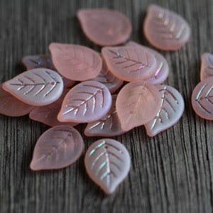May include: A collection of pink glass leaf-shaped beads with a iridescent finish. The beads have a delicate etched design and are perfect for jewelry making or crafting.
