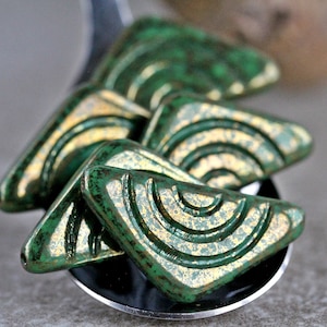 May include: Four green and gold triangular ceramic tiles with a textured surface and a concentric circle design.