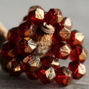 May include: A close-up of a strand of red and gold glass beads. The beads are faceted and have a metallic sheen. The beads are arranged in a circular pattern.
