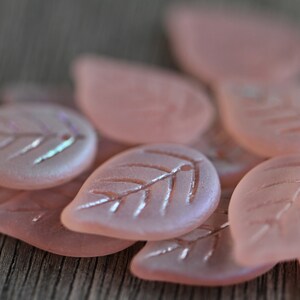 May include: A collection of pink glass leaf-shaped beads with a frosted finish and iridescent accents.