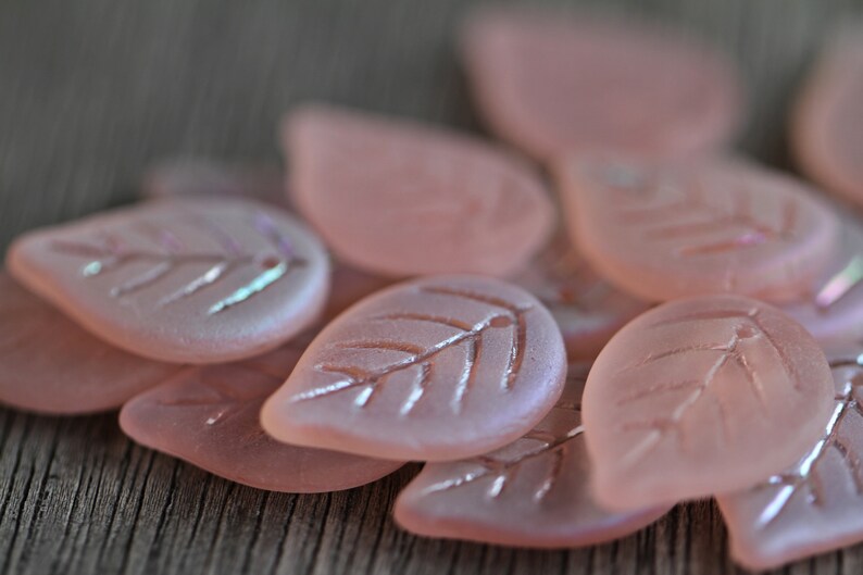 May include: A collection of pink glass leaf-shaped beads with a frosted finish and iridescent accents.
