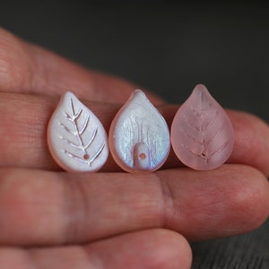 May include: Three leaf-shaped beads, one white with a silver leaf design, one iridescent white, and one pink.