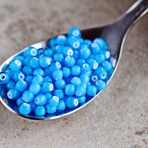 Puede incluir: Una cuchara de plata llena de peque&ntilde;as cuentas de vidrio azul claro con centros blancos.