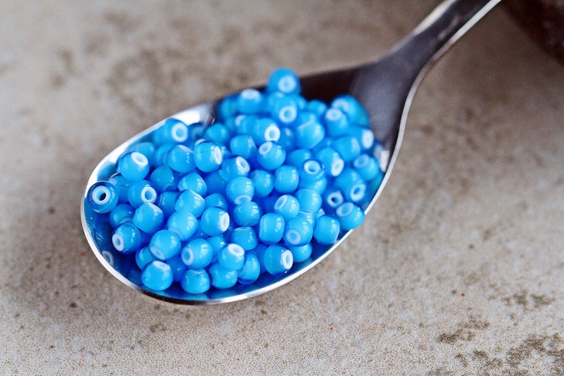 Puede incluir: Una cuchara de plata llena de peque&ntilde;as cuentas de vidrio azul claro con centros blancos.